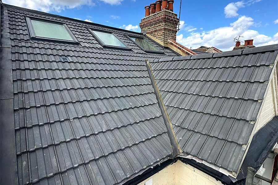 A grey tiled terrace roof with its chimney stack and pots against a blue sky