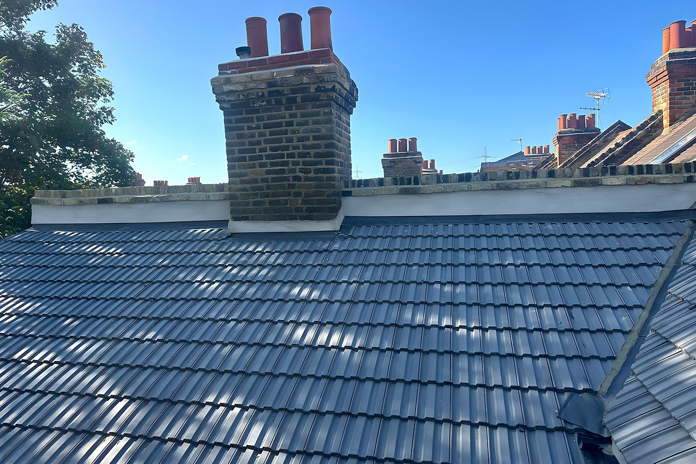 A finished tiled roof and rebuilt chimney stack under a blue sky